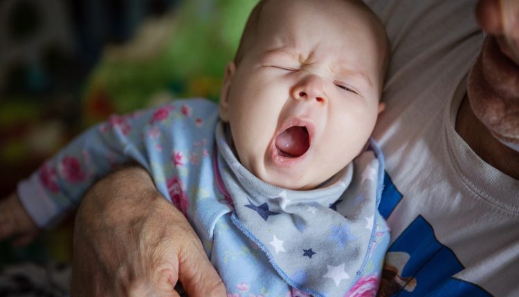 Baby girl yawning. Grandfather rocking baby to sleep.